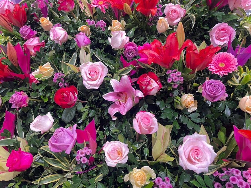 Eine weiße Kerze neben weißen Rosen und einer kleinen Urne auf einem Holztisch