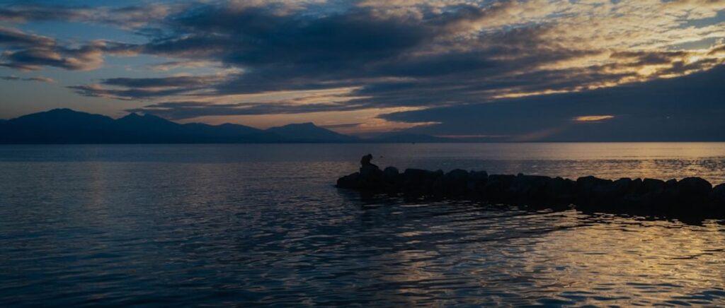 Eine einzelne weiße Blume auf der Wasseroberfläche eines ruhigen Meeres bei Sonnenuntergang