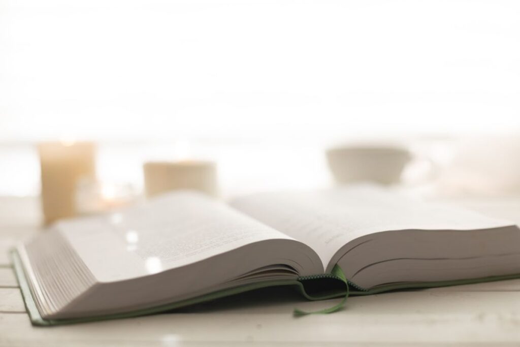 Weiße Kerze auf Holztisch neben geschlossenem Buch