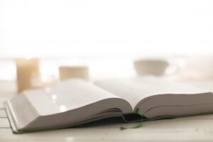 Weiße Kerze auf Holztisch neben geschlossenem Buch